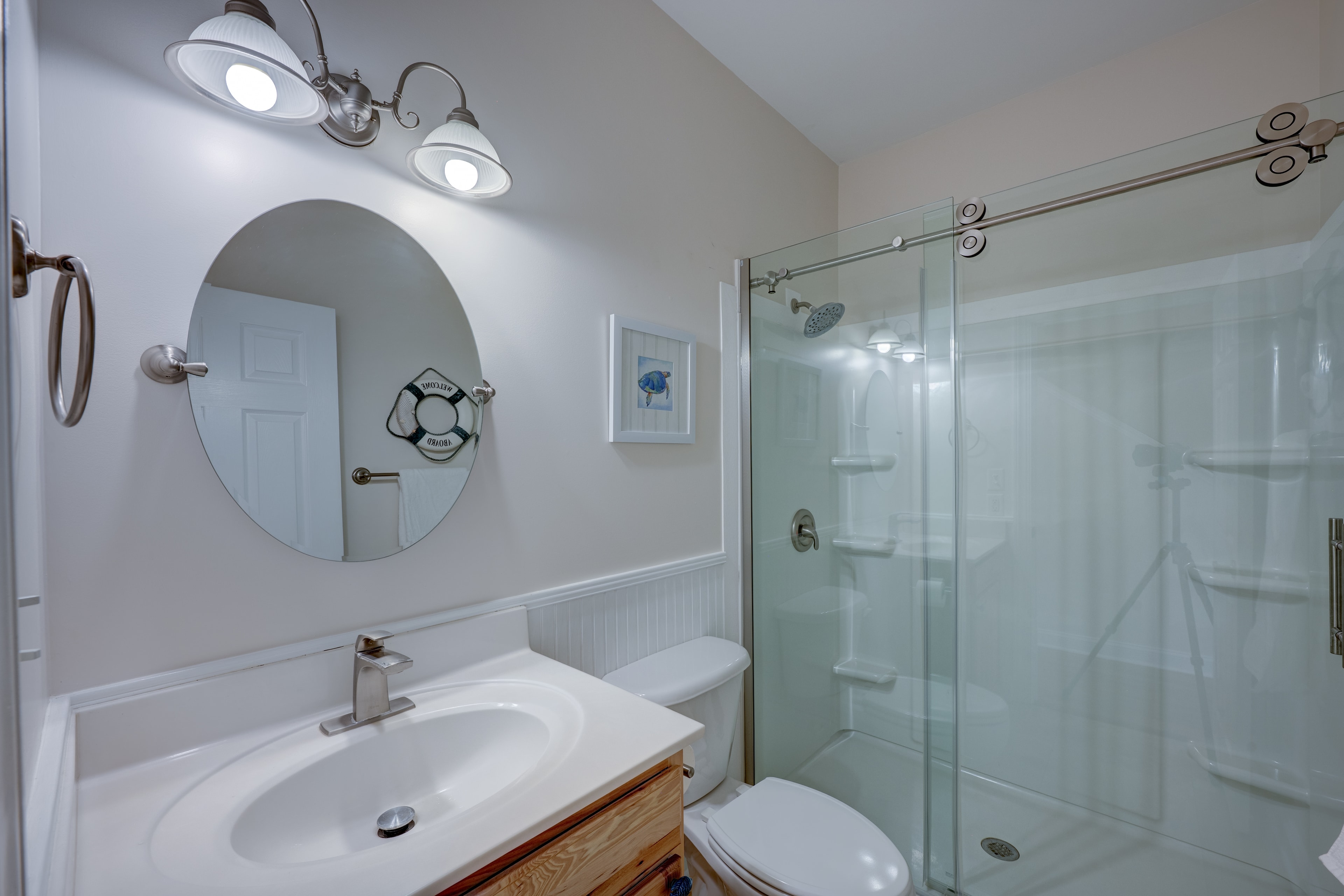 Main level bathroom with oval mirror, glass shower and coastal decor