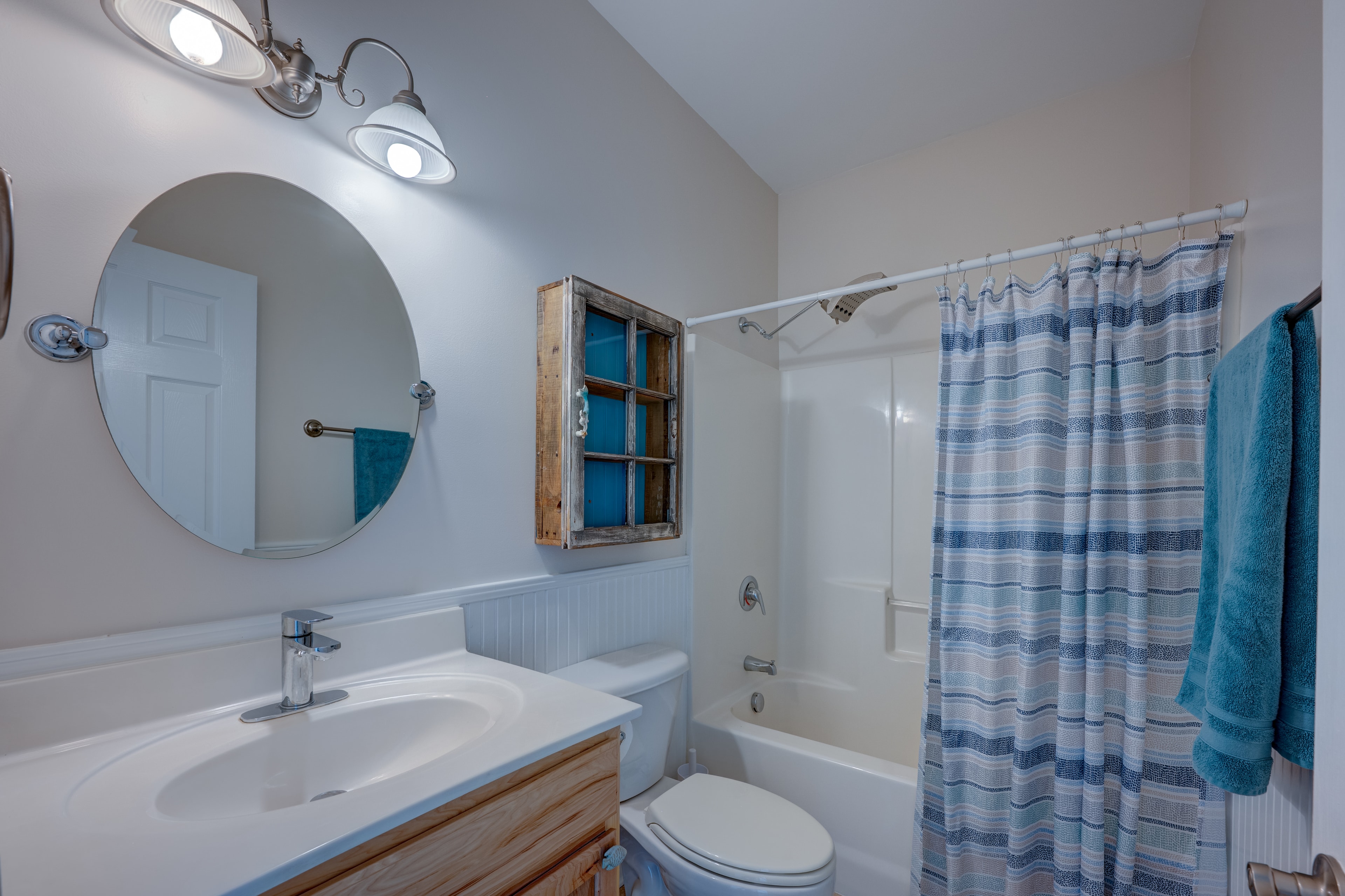 Third bathroom with coastal style, round mirror, teal accents and tub/shower