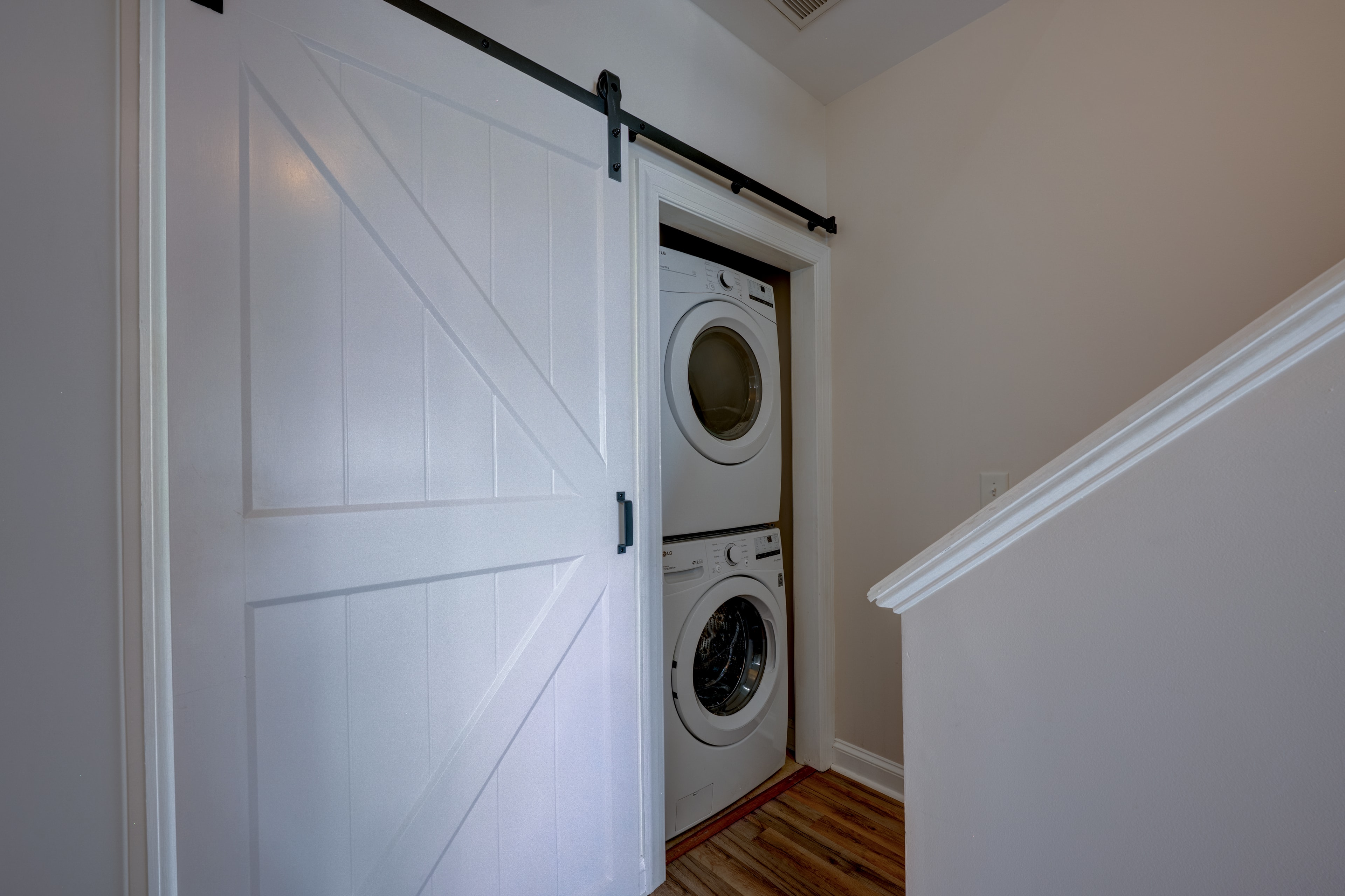 Stackable washer and dryer in laundry closet with white barn door